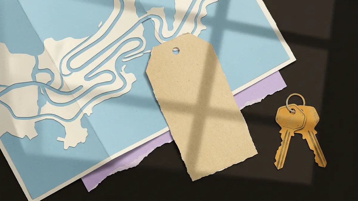 A blank luggage tag, a folded map, and brass keys resting on a wooden table with window light shadows.