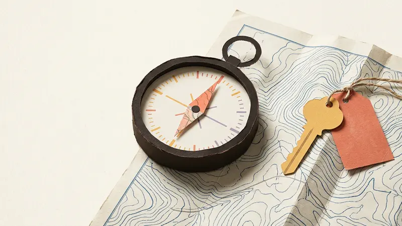 An old compass and a brass room key resting on a folded topographical map in bright natural light.
